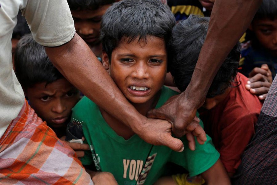 Rohingya refugee children are stopped by volunteers as they jostle to receive food distributed by local organizations in Kutupalong, Bangladesh, September 9, 2017. Reuters