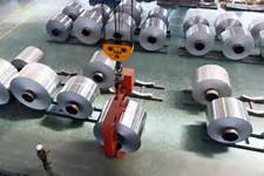 An employee looks at an aluminium foil roll being lifted at a plant in Binzhou, Shandong province, China.                                                            	— Reuters