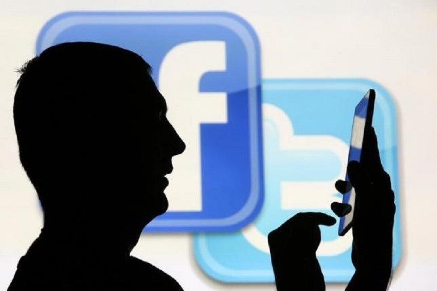 A man is silhouetted as he uses a mini tablet computer while standing in front of a video screen with the Facebook and Twitter logos, in this picture illustration taken in Sarajevo October 22, 2013. Reuters/Files