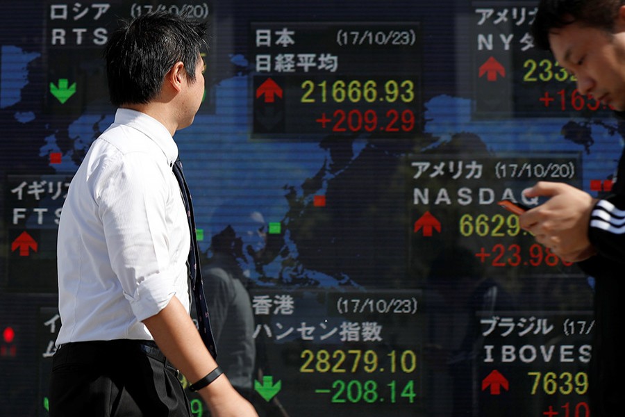 Passersby walk past an electronic board showing market indices outside a brokerage in Tokyo, Japan on October 23 last. - Reuters