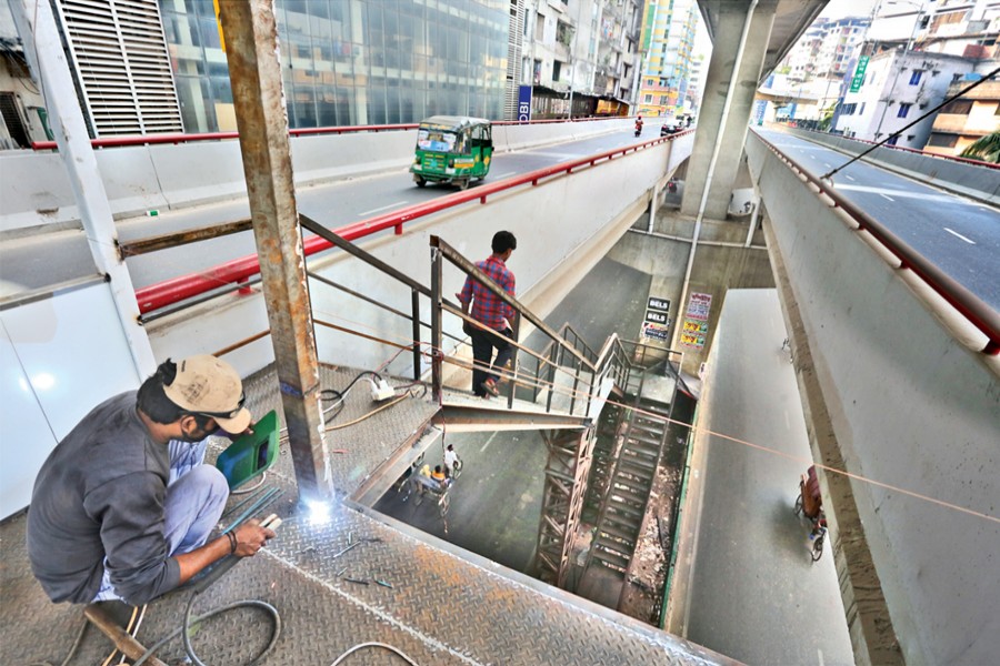 Workers instal steel-made stairs being added to the Mogbazar-Mouchak Flyover in the capital on Friday to facilitate supervision by law-enforcers. It is beyond the design of the infrastructure.	— FE Photo by KAZ Sumon