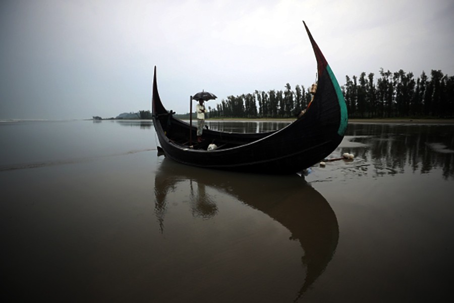 A man holds an umbrella as he stands on a boat, which capsized with a group of Rohingya refugees at Bailakhali, near Cox's Bazar last year. -Reuters file photo