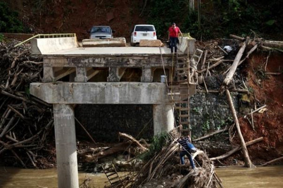 A woman looks as her husband climbs down a ladder at a partially destroyed bridge, after Hurricane Maria hit the area in September, in Utuado, Puerto Rico November 9, 2017. Reuters/Files