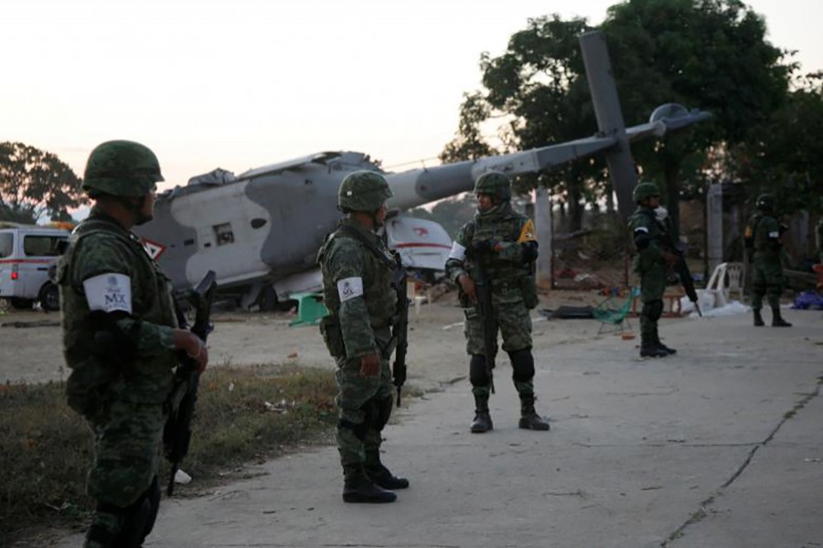 Soldiers stand guard next to a military helicopter crashed on top of two vans in an open field on Saturday while trying to land in Santiago Jamiltepec, Mexico. - Reuters photo