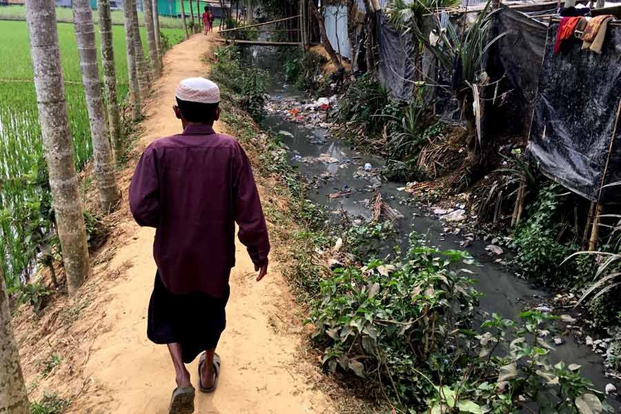 A man walks between a rice field and the shacks of Rohingya refugees living on the land of Bangladeshi farmer Jorina Katun near the Kutapalong refugee camp in Cox's Bazar recently. -Reuters photo