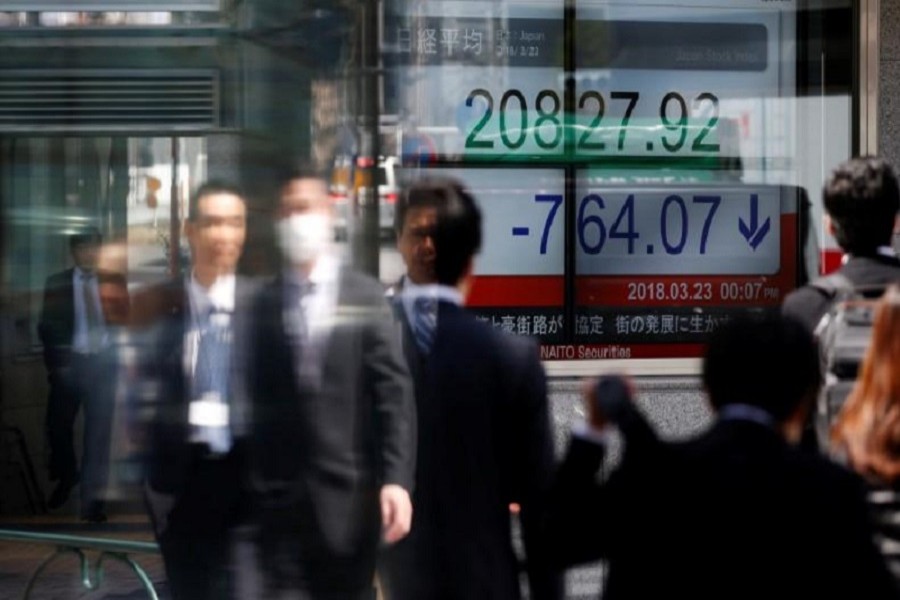 People walk past an electronic board showing Japan's Nikkei average outside a brokerage in Tokyo, Japan, March 23, 2018. Reuters/FiIe Photo