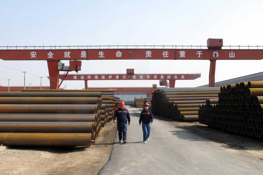 Workers walk past steel pipes at a steel mill in Cangzhou, Hebei province, China March 19, 2018. Reuters/File Photo