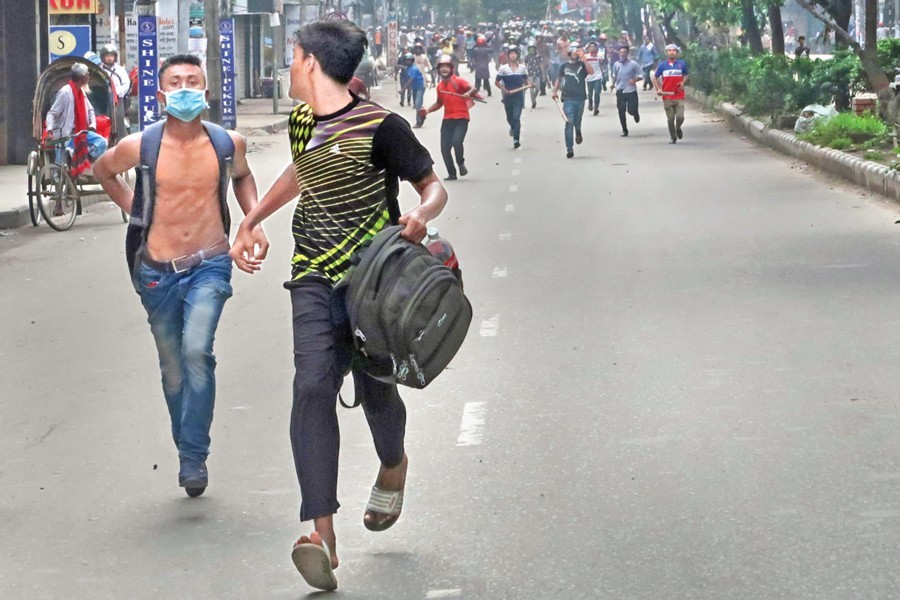 Two student demonstrators running for cover to protect themselves from a contingent of helmet-worn youths, also armed with sticks, in the capital's Elephant Road area on Sunday. — FE Photo by Shafiqul Alam