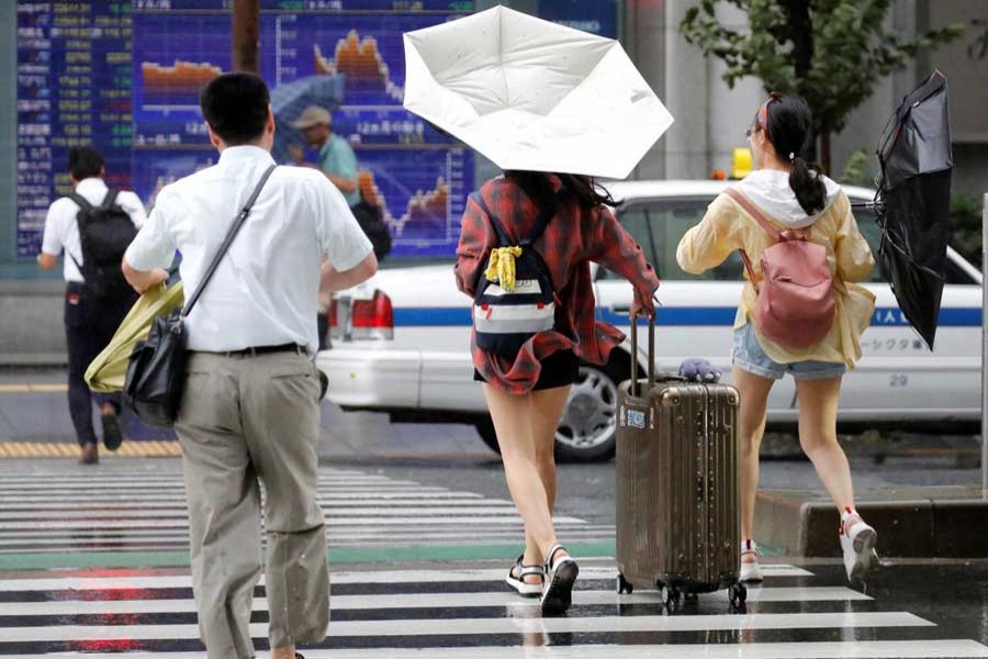 Passersby using umbrellas struggle against a heavy rain and wind in front of an electronic stock quotation board as Typhoon Shanshan approaches Japan's mainland in Tokyo, Japan August 8, 2018. Reuters