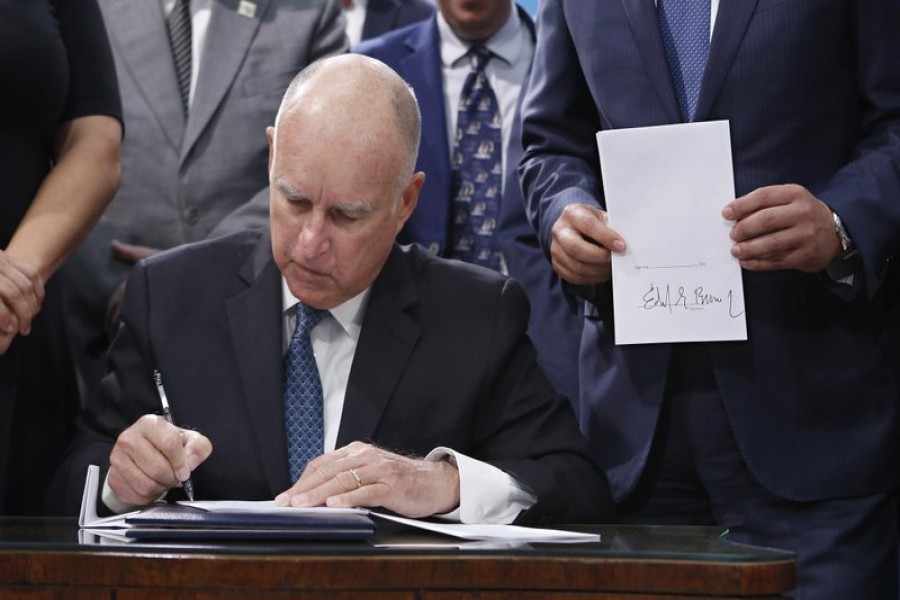 Governor Jerry Brown, signs a copy of the environmental measure SB100 as the bill's author, state Sen. Kevin de Leon, right, holds a copy of the bill, Monday, Sept. 10, 2018, in Sacramento, California. - AP