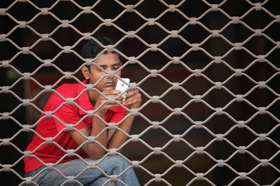 A youth browses his mobile phone while waiting in Dhaka. Photo: ADB