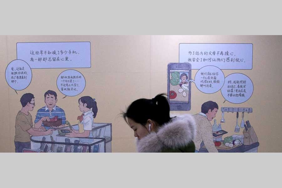 A woman browses her iPhone as she walks by a mural depicting an iPhone and Chinese people buy smartphone to communicate with family members, at a subway station in Beijing, Thursday, Jan 3, 2019.