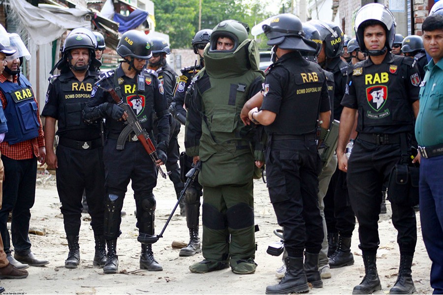 RAB officials, along with a member of bomb disposal unit, wait outside a tin-roofed house in Mohammadpur’s Basila as they prepare to enter the suspected militant hideout — Focus Bangla photo