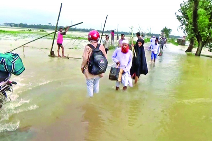 People wading through floodwater on a road in Netrakona on Saturday