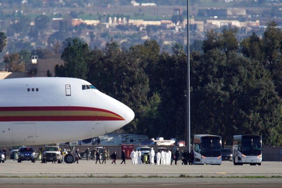 Passengers board buses past personnel in protective clothing after arriving on an aircraft, chartered by the US State Department to evacuate government employees and other Americans from the novel coronavirus threat in the Chinese city of Wuhan, at March Air Reserve Base in Riverside County, California, US, January 29, 2020. Reuters