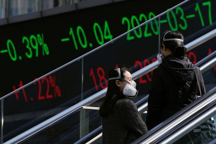 Pedestrians wearing protective masks ride an escalator near an overpass with an electronic board showing stock information, following an outbreak of the coronavirus disease (COVID-19), at Lujiazui financial district in Shanghai, China, March 17, 2020. — Reuters