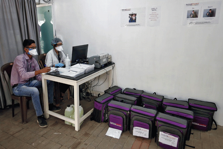 Laboratory technicians sit next to boxes containing coronavirus testing kits at a sample collection centre in Ahmedabad, India. --Reuters