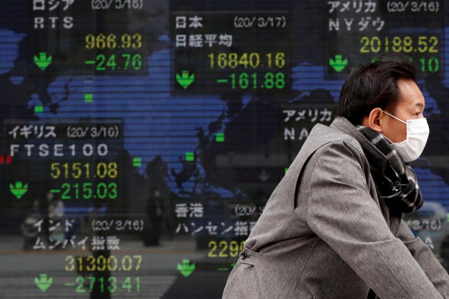 A man wearing a protective face mask following an outbreak of the coronavirus disease (COVID-19) walks past a screen displaying the world's markets indices outside a brokerage in Tokyo, Japan on March 17, 2020 — Reuters/Files