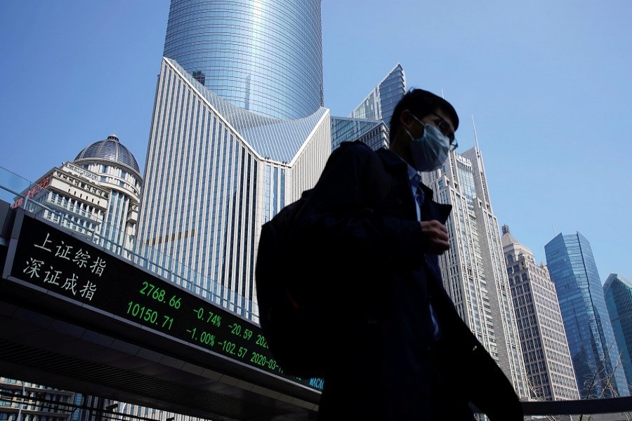 A pedestrian wearing a face mask walks near an overpass with an electronic board showing stock information, following an outbreak of the coronavirus disease (COVID-19), at Lujiazui financial district in Shanghai, China, March 17, 2020. — Reuters/Files