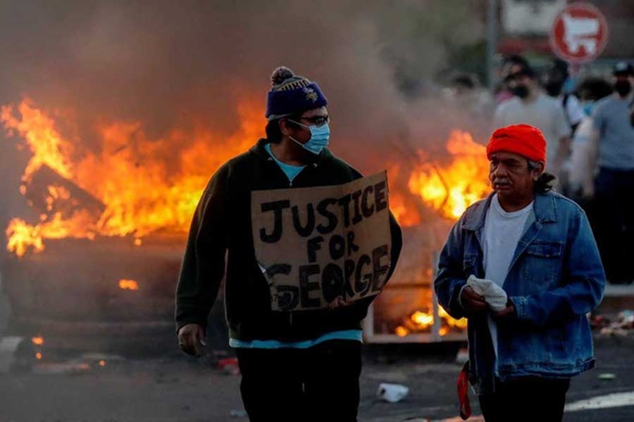 A man holding a sign near a burning vehicle at the parking lot of a Target store during protests after a white police officer was caught on a bystander's video pressing his knee into the neck of African-American man George Floyd, who later died at a hospital, in Minneapolis, Minnesota of US on Thursday. –Reuters Photo