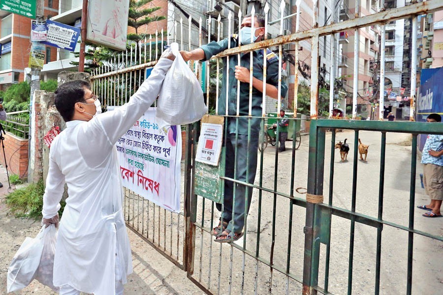 Essential items being sent to houses through security men at East Rajabazar near Green Road in the city on Wednesday after the area came under lockdown from Tuesday midnight — FE photo by KAZ Sumon