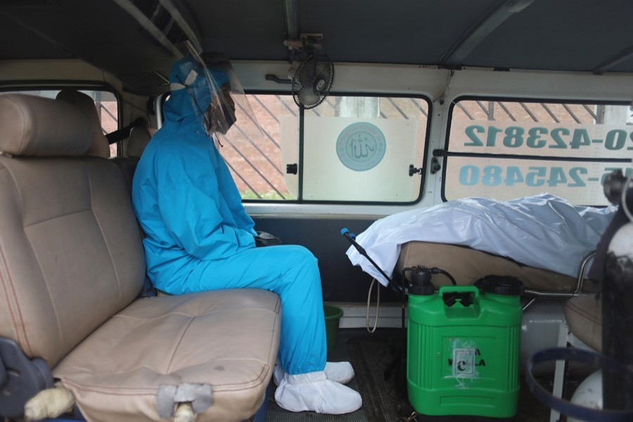 A health worker wearing protective suits sits inside an ambulance that carrying the dead body of a victim who died with Covid-19 symptoms in Dhaka