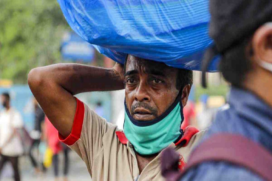 A man with a face mask on his chin carries a load on his head as he walks to catch a bus in Kolkata, India