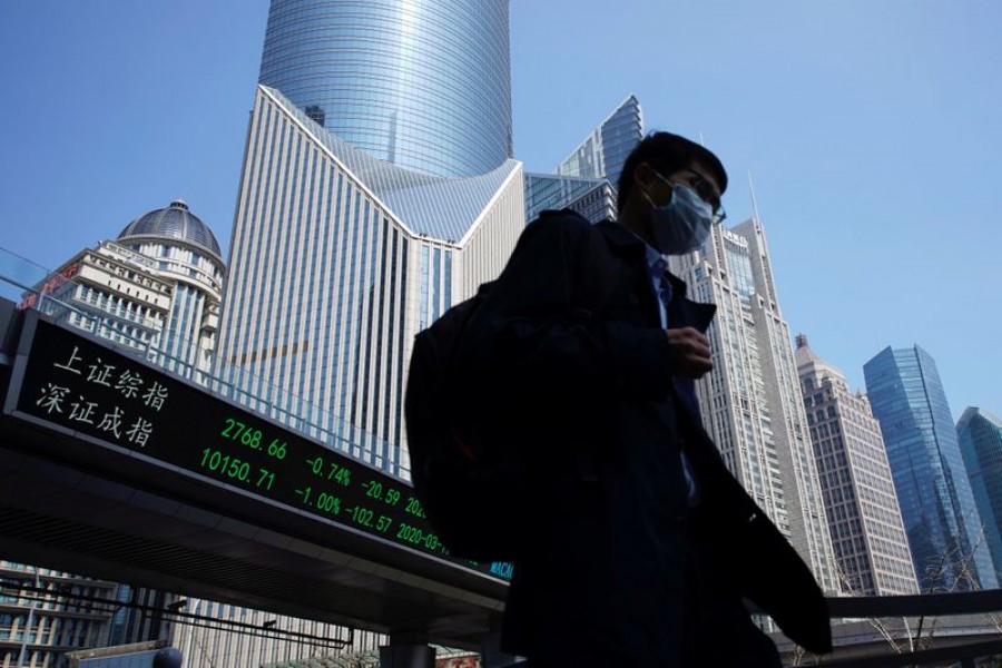 A pedestrian wearing a face mask walks near an overpass with an electronic board showing stock information, following an outbreak of the coronavirus disease (Covid-19), at Lujiazui financial district in Shanghai, China March 17, 2020. REUTERS/Aly Song