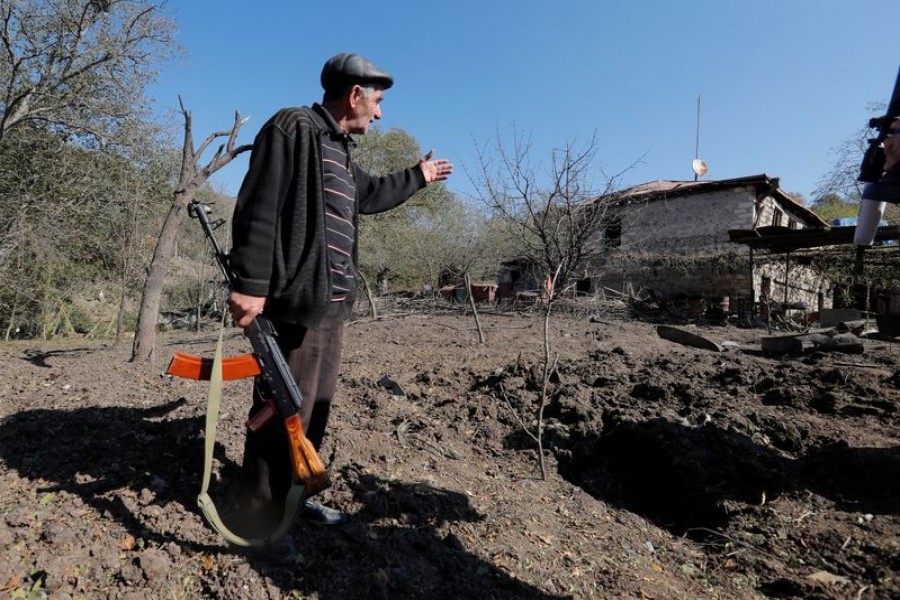 Local resident Alexei Agadzhanov holds a rifle while showing a crater following recent shelling in the settlement of Shosh in the course of a military conflict over the breakaway region of Nagorno-Karabakh on October 17, 2020 — Reuters/Stringer