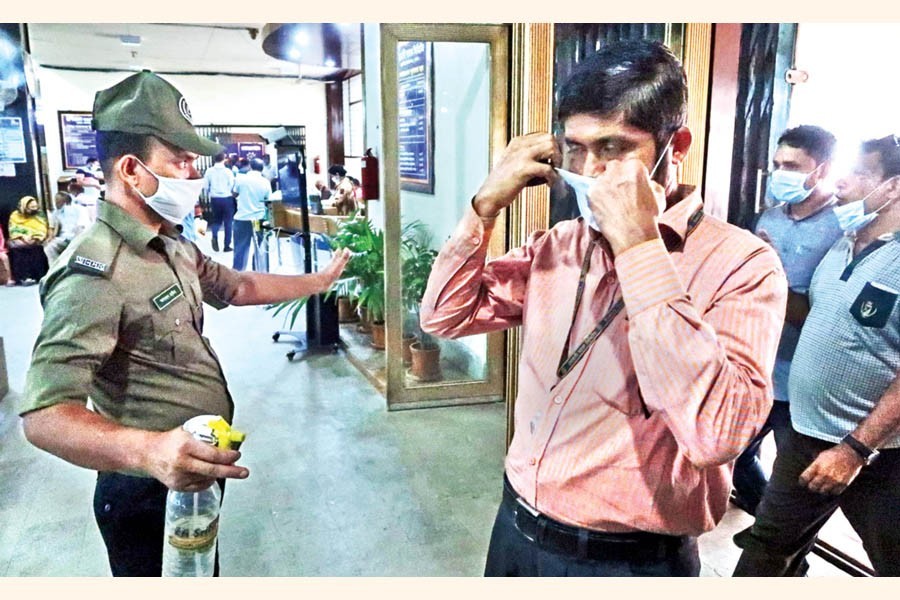 With 'No mask, no service' policy in effect at all offices, a security guard makes a person wear his mask before he enters the Sonali Bank at Motijheel in the city on Tuesday — FE photo by Shafiqul Alam