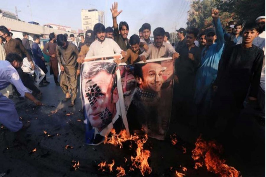 People chant slogans as they set fire to a banner with an image of French President Emmanuel Macron during a protest against cartoon publications of Prophet Mohammad in France and French President Emmanuel Macron's comments, in Peshawar, Pakistan Oct 27, 2020. REUTERS