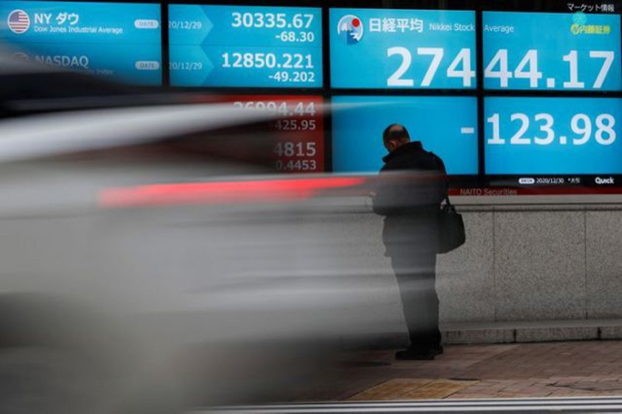 A man stands in front of a screen displaying Nikkei share average and the world's stock indexes outside a brokerage, amid the coronavirus disease (Covid-19) outbreak, in Tokyo, Japan on December 30, 2020 — Reuters/Files