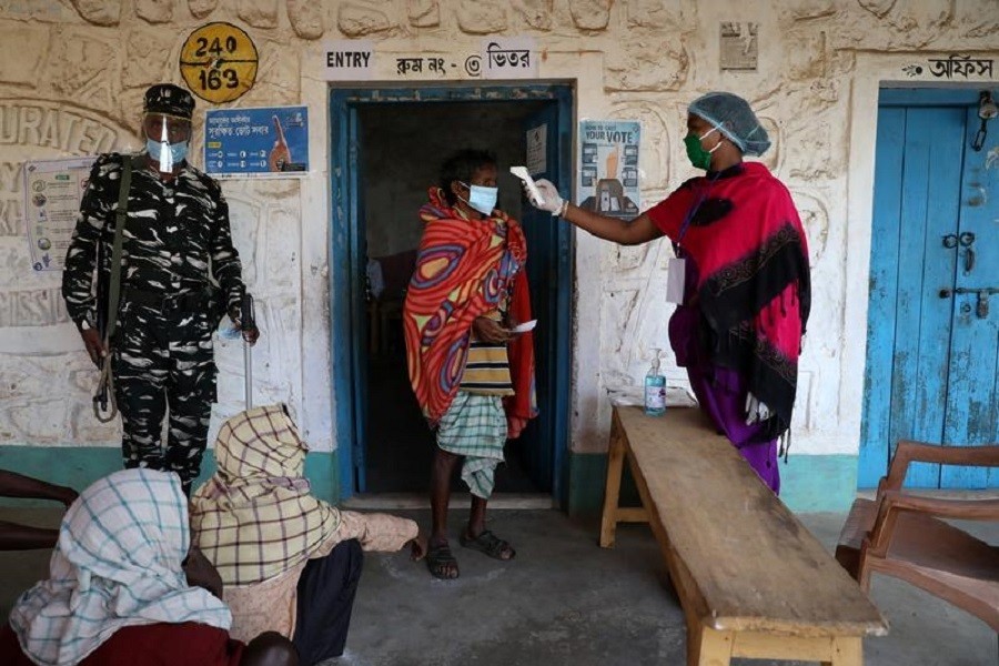 A woman checks the temperature of a voter before he casts his vote at a polling booth during the first phase of the West Bengal state election in Purulia district, India, March 27, 2021 — Reuters