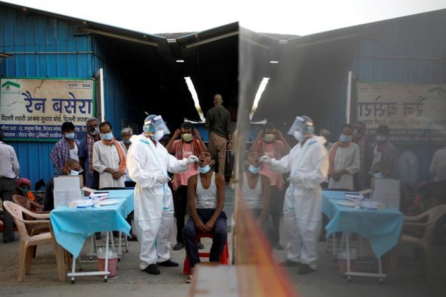 FILE PHOTO: A healthcare worker collects a coronavirus disease (COVID-19) test swab sample from a man as others watch, at a temporary shelter for the homeless in New Delhi, India, March 31, 2021. REUTERS/Adnan Abidi