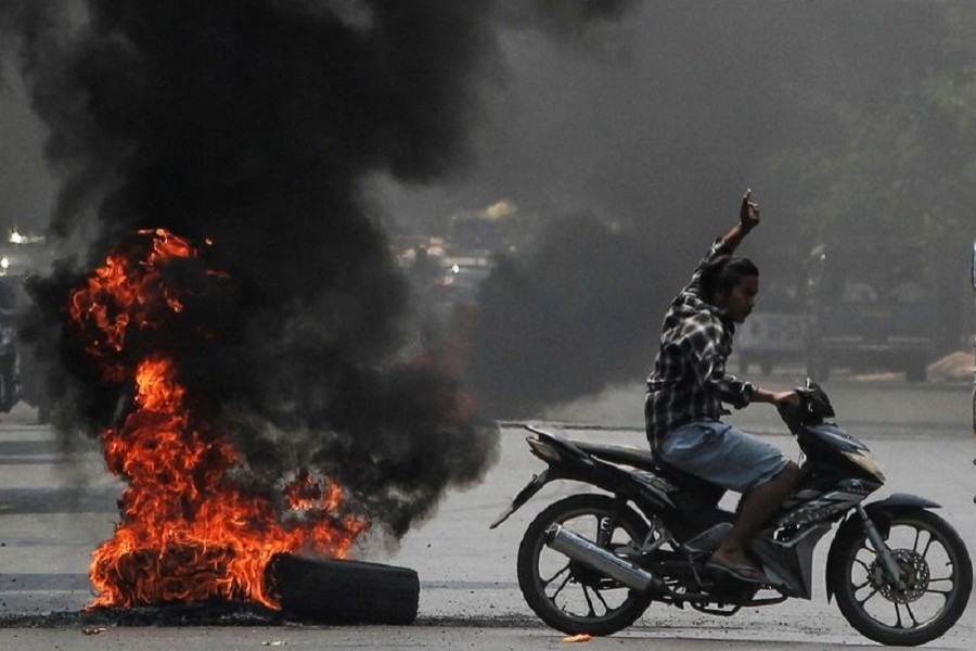 A man flashes the three-finger salute as he passes burning tires during a protest against the military coup, in Mandalay, Myanmar, April 1, 2021 — Reuters/Stringer