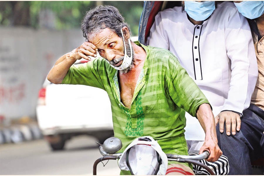 A rickshawpuller wipes sweat from his forehead in the summer heat as he carries passengers on his rickshaw passing through the Dhaka University campus on Wednesday — FE photo by Shafiqul Alam