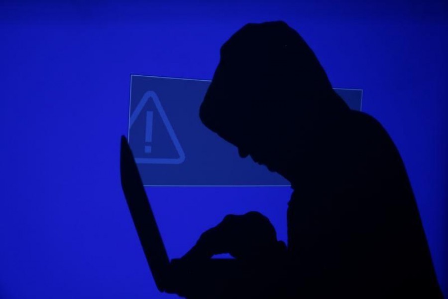 A hooded man holds a laptop computer as blue screen with an exclamation mark is projected on him in this illustration picture taken on May 13, 2017 — Reuters/Files