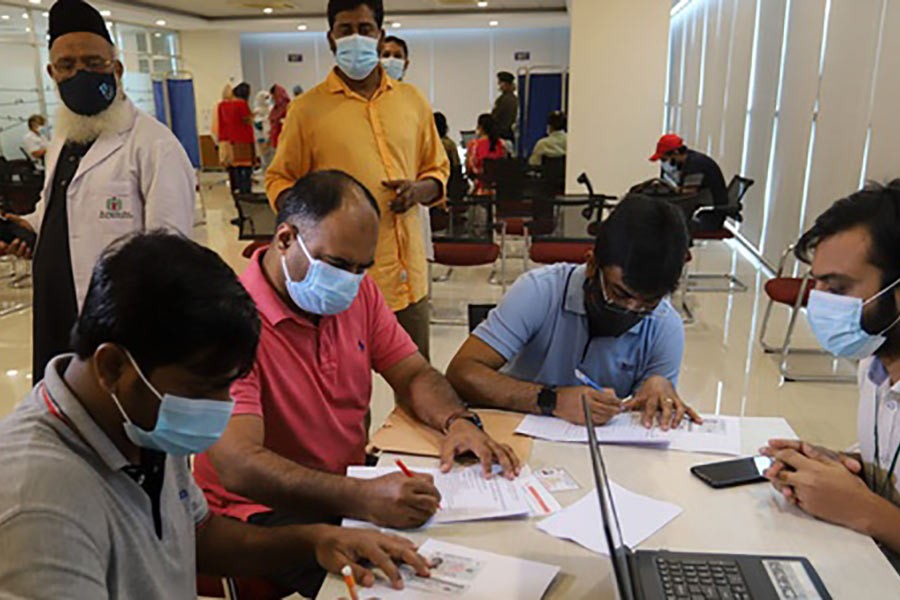 People fill in forms before receiving Pfizer-BioNTech COVID-19 vaccine jabs at Bangabandhu Sheikh Mujib Medical University in Dhaka on Thursday -bdnews24.com photo