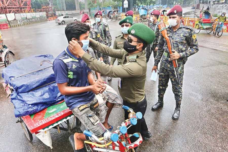 A member of a law enforcement agency giving a mask to a rickshaw puller on a street at Kawran Bazar in Dhaka on Friday — FE file photo