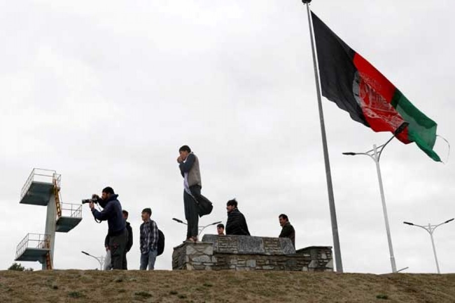 Youths take pictures next to an Afghan flag on a hilltop overlooking Kabul, Afghanistan, April 15, 2021 — Reuters