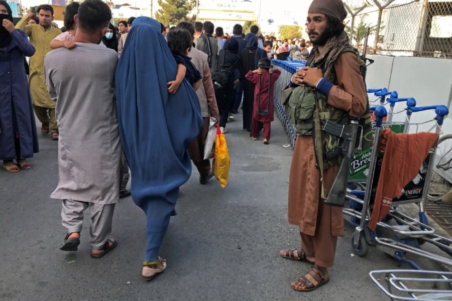 A Taliban fighter stands guard as people walk past at the entrance of Hamid Karzai International Airport - Reuters