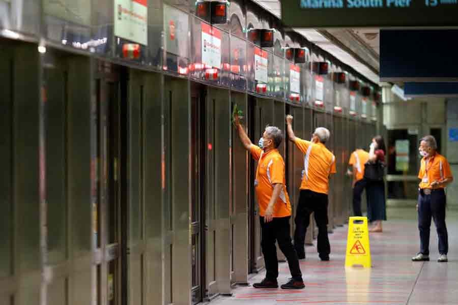 Workers wiping down doors at a train station during the coronavirus disease (COVID-19) outbreak in Singapore on August 17 last year -Reuters file photo