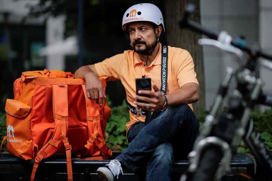 Former Afghan Communication Minister Sayed Sadaat sitting in his orange uniform next to his bike on Wednesday as he works for a food delivery service in Leipzig of Germany -Reuters Photo