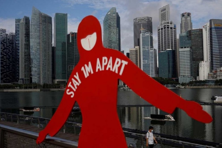 A man wearing a face mask passes a sign put up to encourage social distancing during the coronavirus disease (COVID-19) outbreak, at Marina Bay in Singapore, September 22, 2021. Reuters