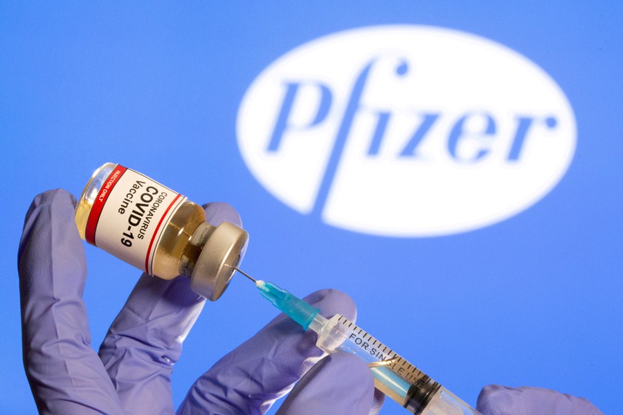 A woman holds a small bottle labeled with a "Coronavirus COVID-19 Vaccine" sticker and a medical syringe in front of displayed Pfizer logo in this illustration taken on October 30, 2020 — Reuters/Files