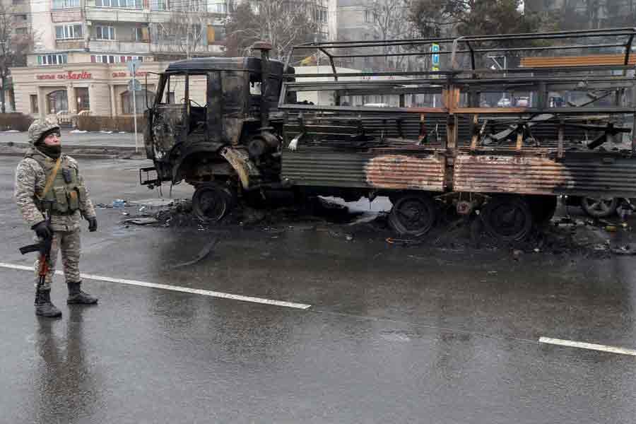 A Kazakh law enforcement officer standing guard near a burnt truck while checking vehicles in a street following mass protests triggered by fuel price increase in Almaty of Kazakhstan on Saturday -Reuters photo