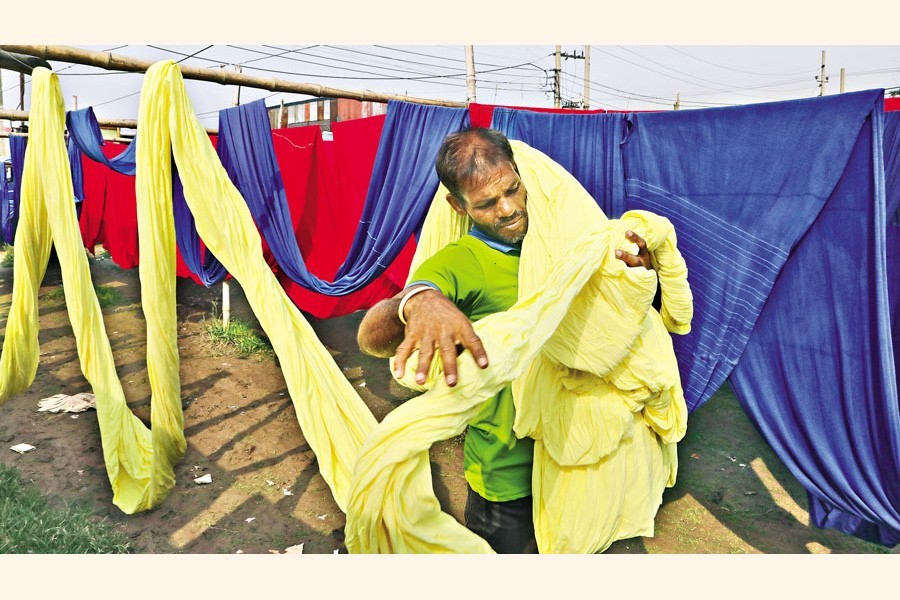 A worker lays sheets of cloth out to dry in Fatullah of Narayanganj on Tuesday. Once the fabrics dry, they are used in the garment factories to make clothes. Though the Bangladesh RMG sector fares well even in this pandemic, calls are being made to include different stakeholders in a committee formed recently to make a unified code of conduct for the sector, in which this worker is also a significant part — FE photo by Shafiqul Alam