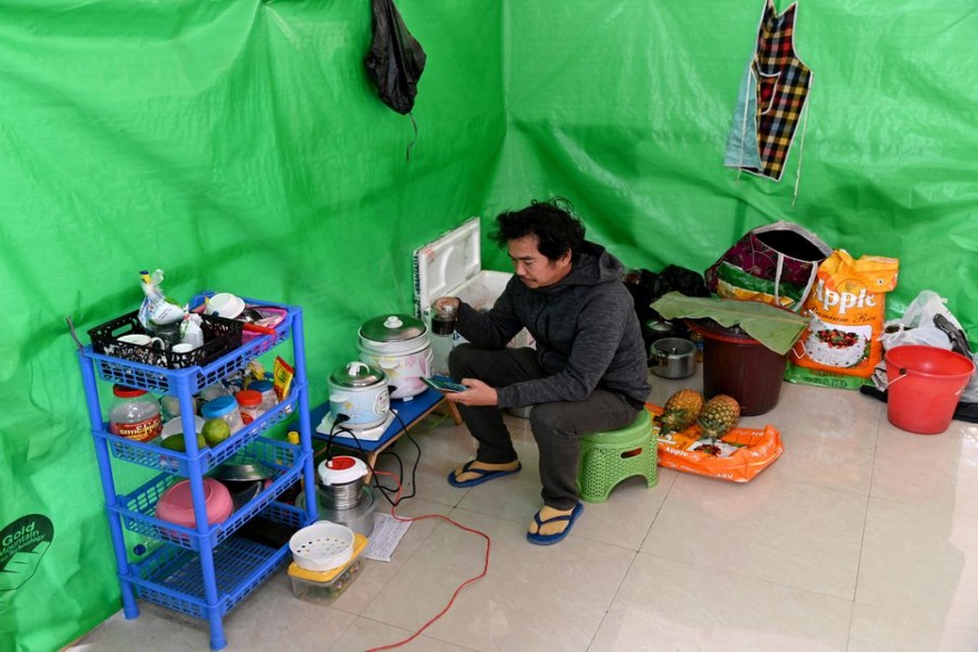 Aung Nay Myo, a protest organiser and satirical writer from Myanmar, drinks tea as he looks at a photo of his father on his phone inside a temporary shelter at an undisclosed location in a town in a country bordering Myanmar, January 27, 2022. REUTERS/Stringer