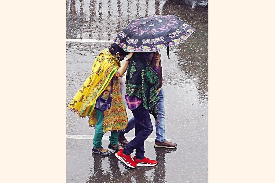 Three people huddle together under an umbrella during rain as they walk down the Elephant Road in the city on Friday — FE photo by KAZ Sumon