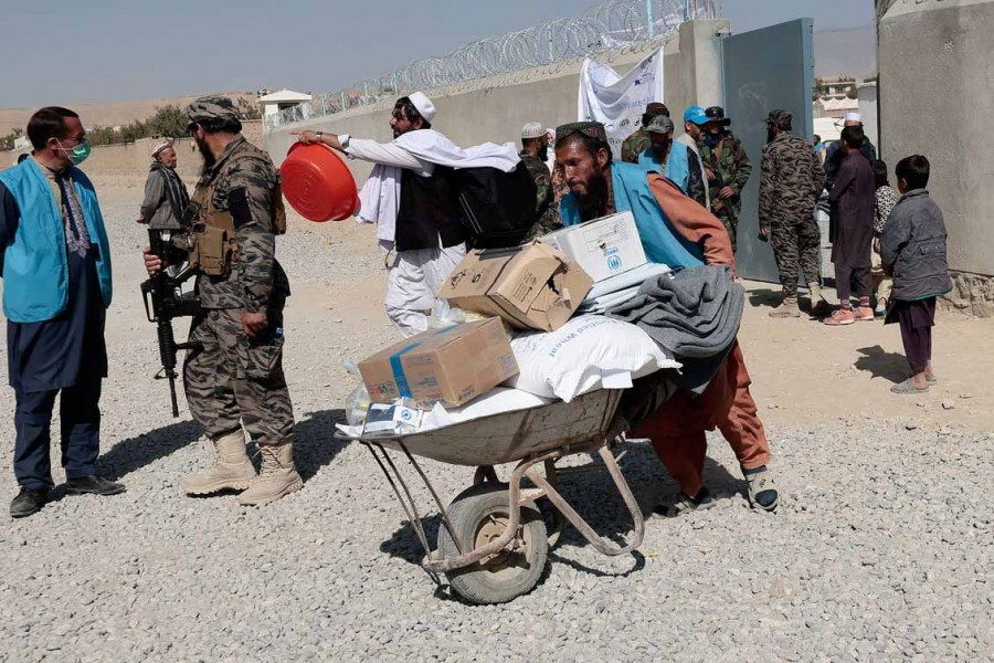 An UNHCR worker pushes a wheelbarrow loaded with aid supplies for a displaced Afghan family outside the distribution center as a Taliban fighter secures the area on the outskirts of Kabul, Afghanistan October 28, 2021 – Reuters/Zohra Bensemra